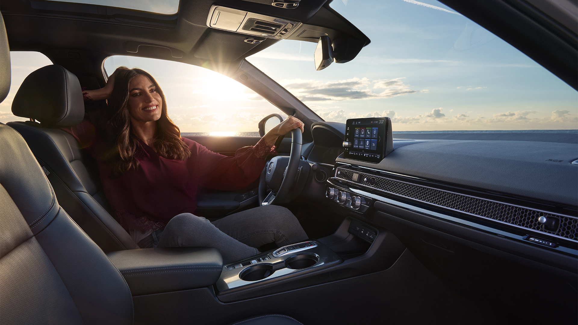 Foto aus dem Innenraum des Civic Hybrid, eine Frau sitzt im Fahrzeug, direkt am Meer.