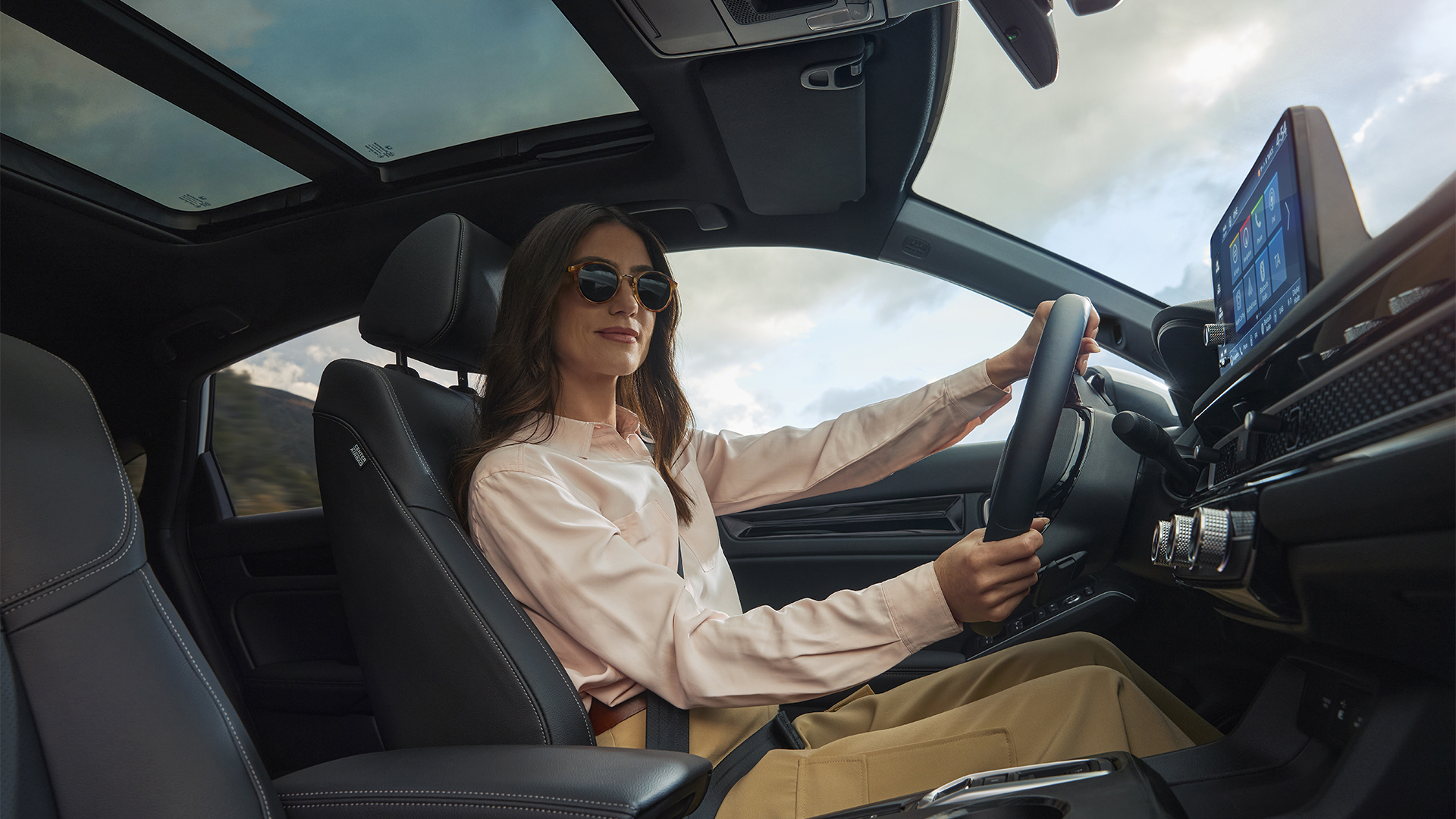 Eine Frau mit Sonnenbrille, die mit den Händen das Lenkrad des Civic Hybrid umfasst