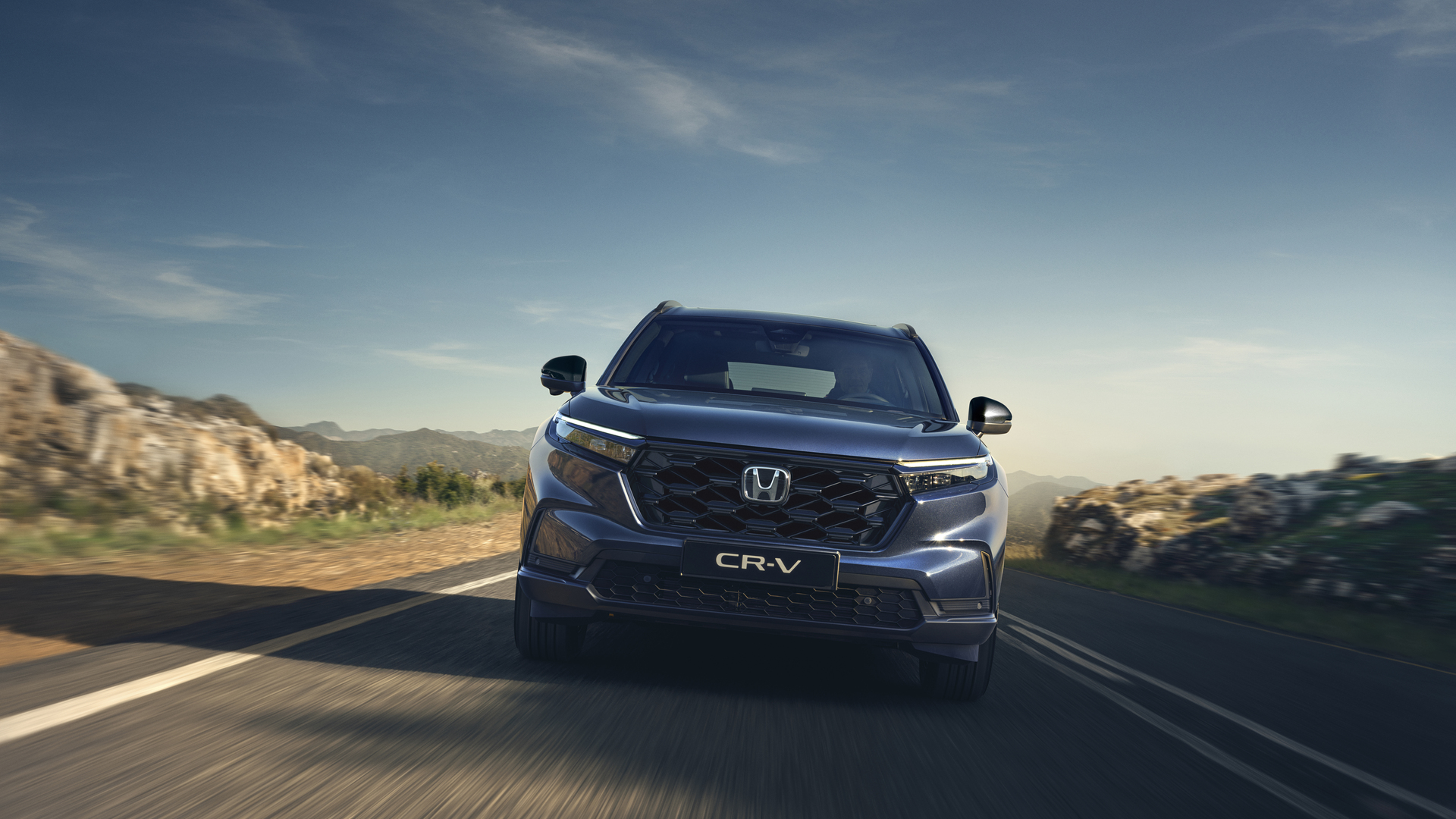 Ein Honda CR-V fährt unter strahlend blauem Himmel eine kurvenreiche Bergstrasse entlang.