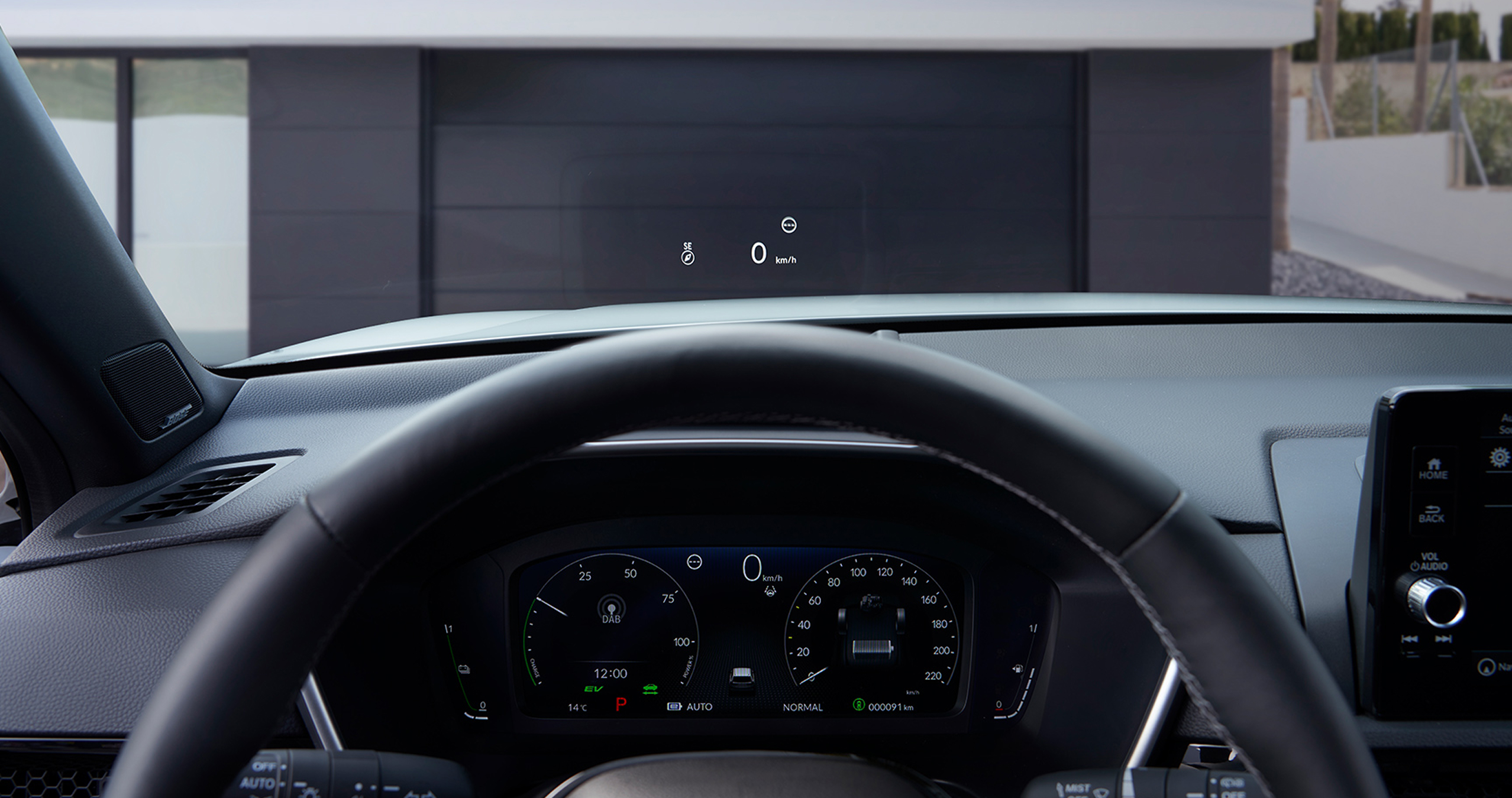 Sicht aus der Fahrerposition mit Head-Up-Display (HUD), das "50 km/h" und einen Kompass auf die Windschutzscheibe über einer Schotterstrasse projiziert.