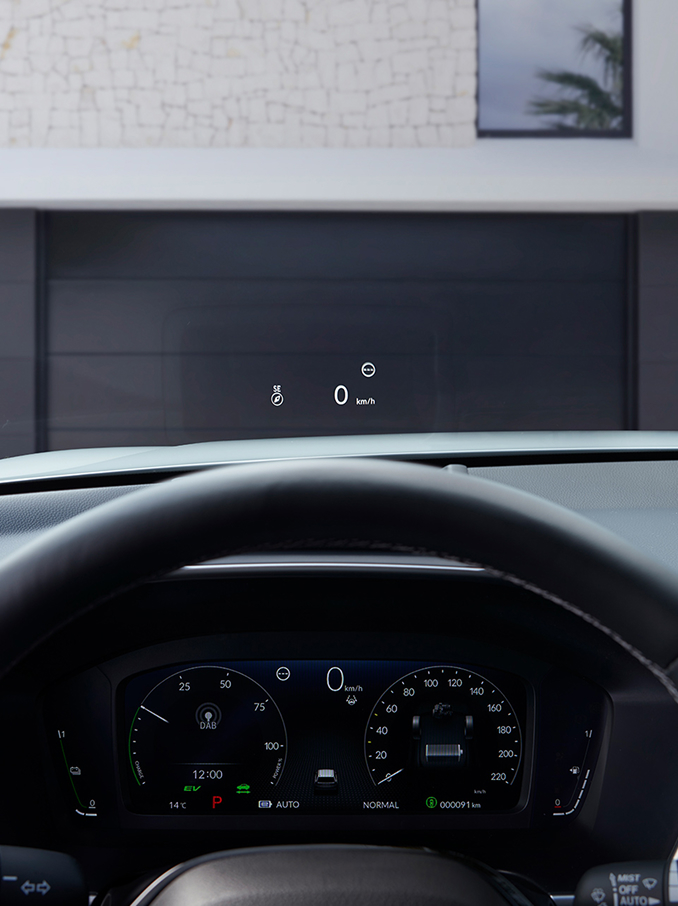 Sicht aus der Fahrerposition mit Head-Up-Display (HUD), das "50 km/h" und einen Kompass auf die Windschutzscheibe über einer Schotterstrasse projiziert.