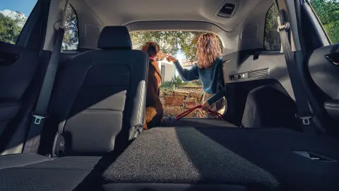 CR-V Hybrid SUV, umgeklappter Rücksitz mit Frau und Hund im offenen Kofferraum. 