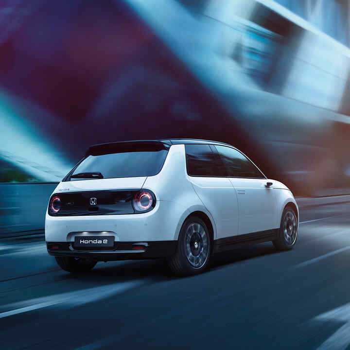 Honda e, 3/4-Heckansicht, in der Stadt fahrend.
