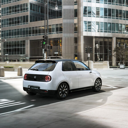 Honda e, 3/4-Heckansicht, in der Stadt fahrend.