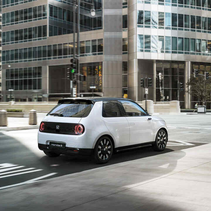 Honda e, 3/4-Heckansicht, in der Stadt fahrend.