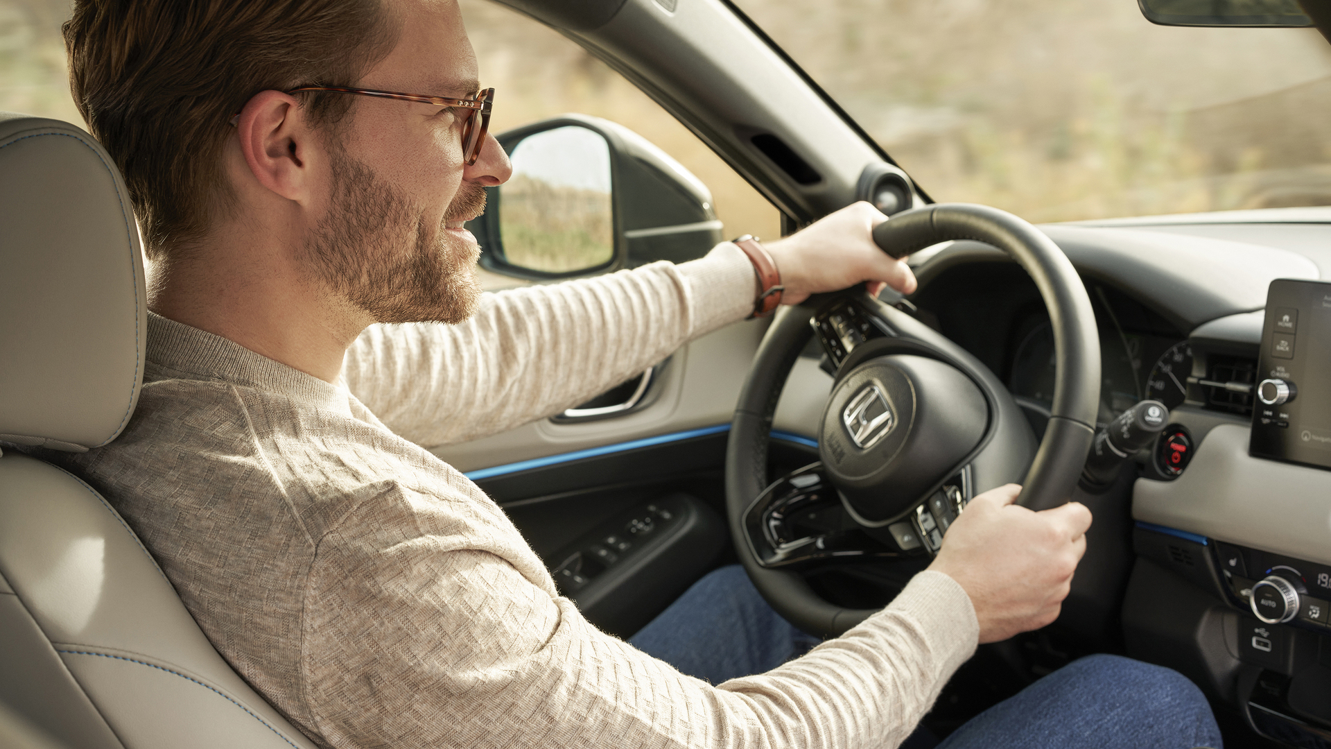 Ein Mann mit Brille fährt einen Honda HR-V; die Aufnahme erfolgt vom Beifahrersitz aus, beide Hände liegen am Lenkrad und das Armaturenbrett ist zu sehen.