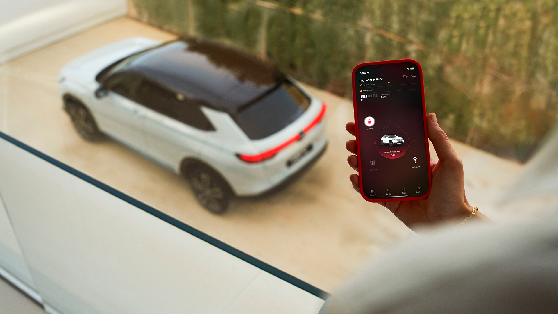 Eine Person hält ein Smartphone, auf dem eine App für Fahrzeugladeeinstellungen angezeigt wird, während im Hintergrund ein weißer SUV geparkt ist.