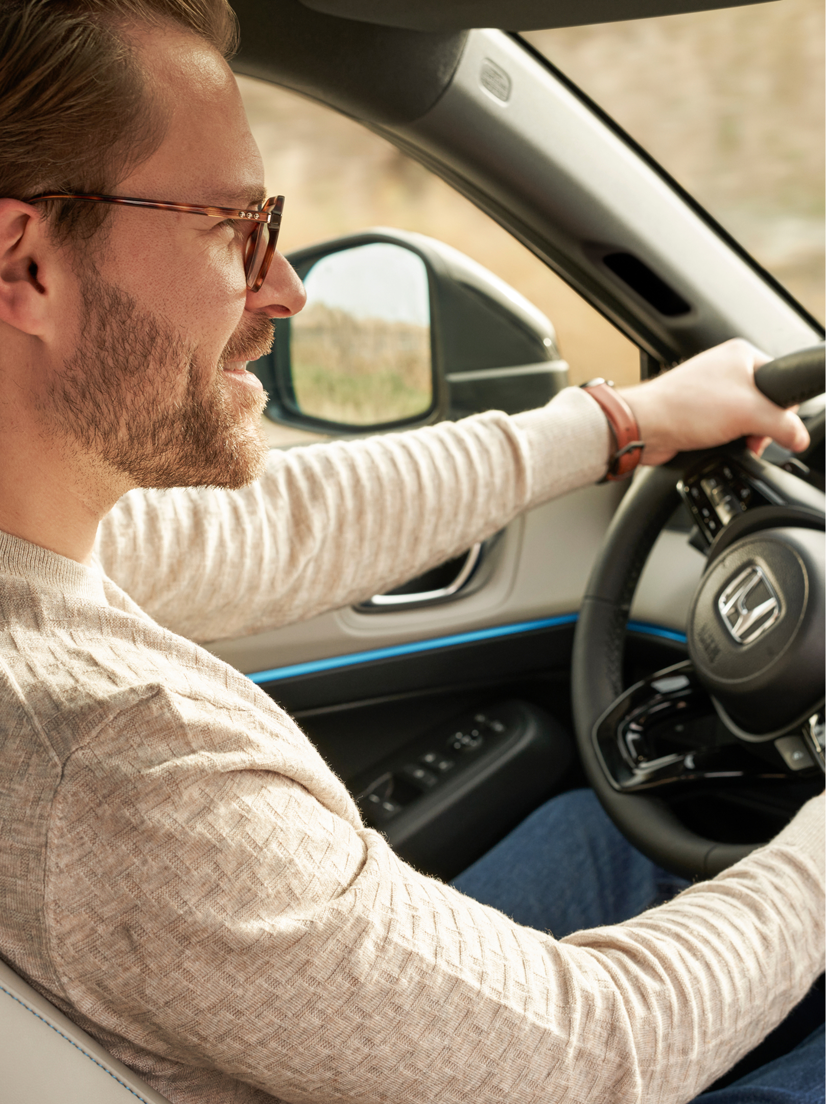 Ein Mann mit Brille fährt einen Honda HR-V; die Aufnahme erfolgt vom Beifahrersitz aus, beide Hände liegen am Lenkrad und das Armaturenbrett ist zu sehen.