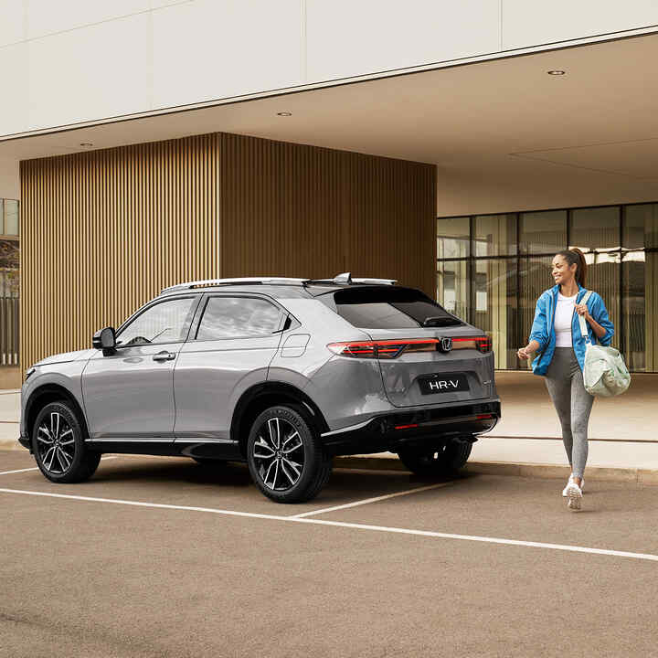 Frau geht an einem geparkten HR-V vorbei. 