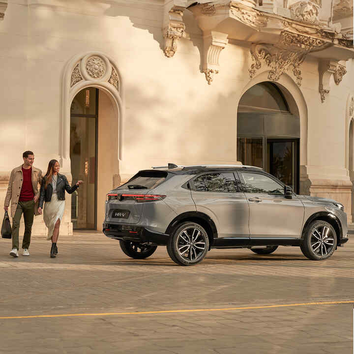 Ein Paar geht neben dem HR-V, der vor einem Gebäude geparkt ist. 
