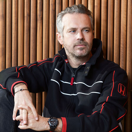 Mann mit Honda Racing Hut und Jacke, der sich an die Hutkrempe tippt.
