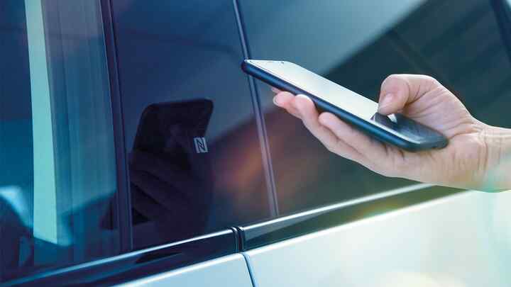 Nahaufnahme einer Person mit Smartphone und My Honda+ App neben seinem Fahrzeug