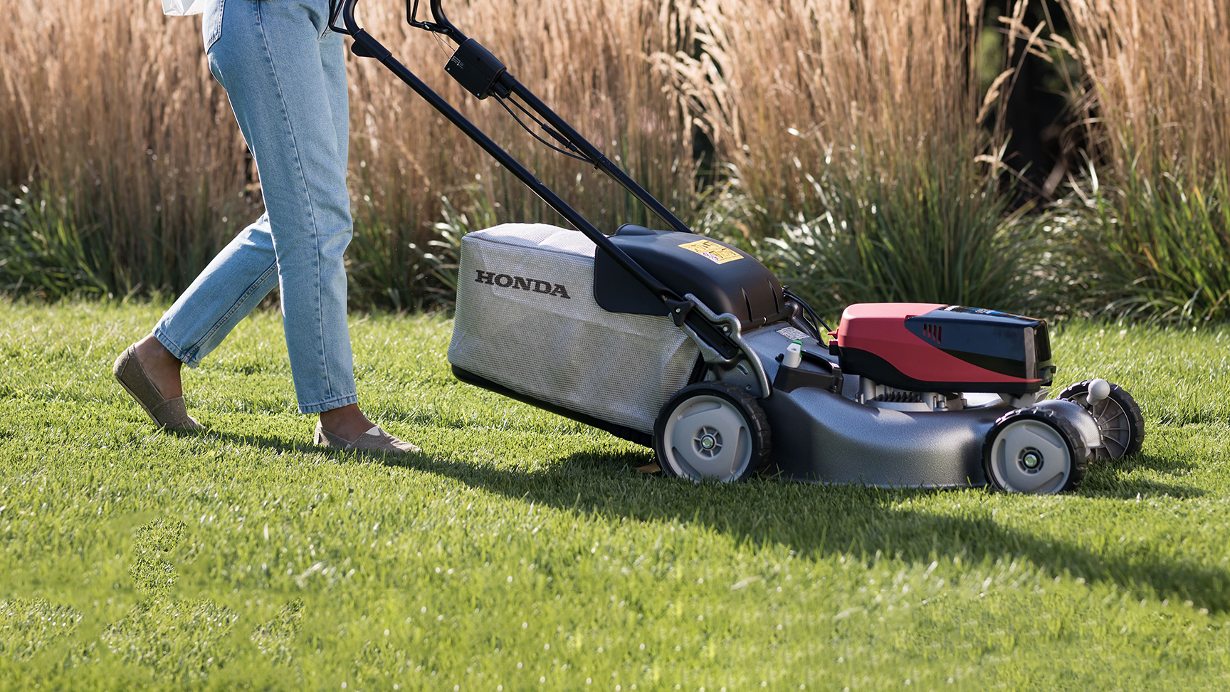 Frau beim Schieben eines IZY-ON Rasenmähers auf dem Rasen.