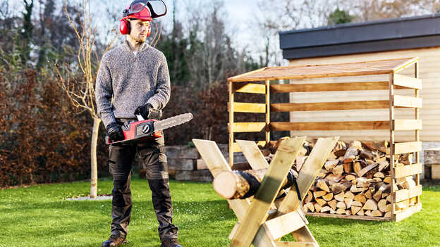 Mann mit Akku-Kettensäge in einem Garten.