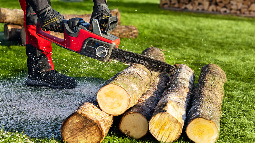 Model beim Holzschneiden mit einer Honda Akku-Kettensäge, Nahaufnahme.