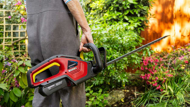 Model mit Honda Akku-Heckenschere in einem Garten.