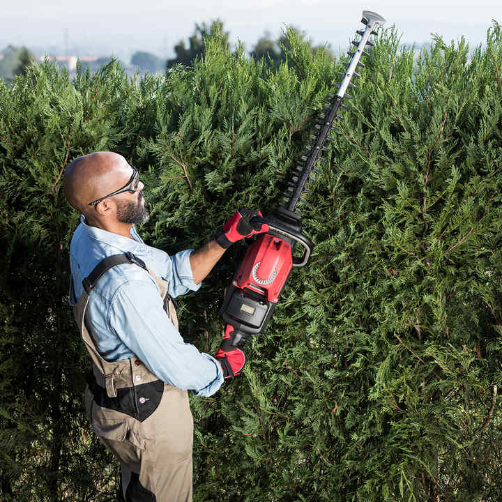 Model using Honda's cordless hedge trimmer in a garden location.