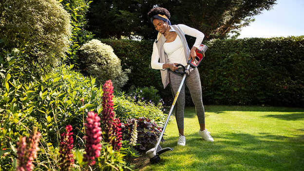 Frau, die den Pflanzenschutz des Honda Akku-Rasentrimmers in einem Garten vorführt.
