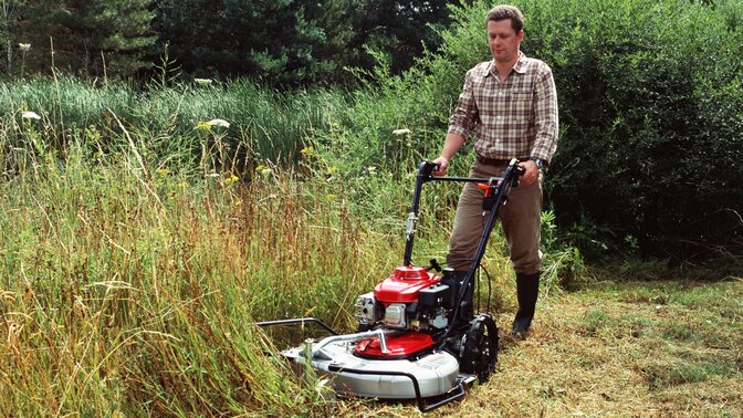 Wiesenmäher in 3/4-Frontansicht, nach links zeigend, Verwendung nach Modell. Gartenumgebung.