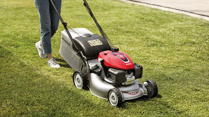 Frau mit Honda IZY Rasenmäher beim Mähen in einem Garten