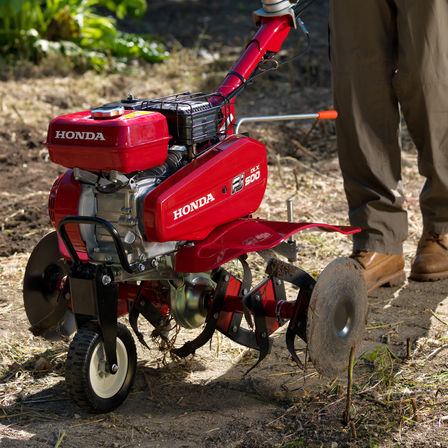 Nahaufnahme der Kompakt-Motorhacke, Fokus auf dem Transportrad, Gartenumgebung.