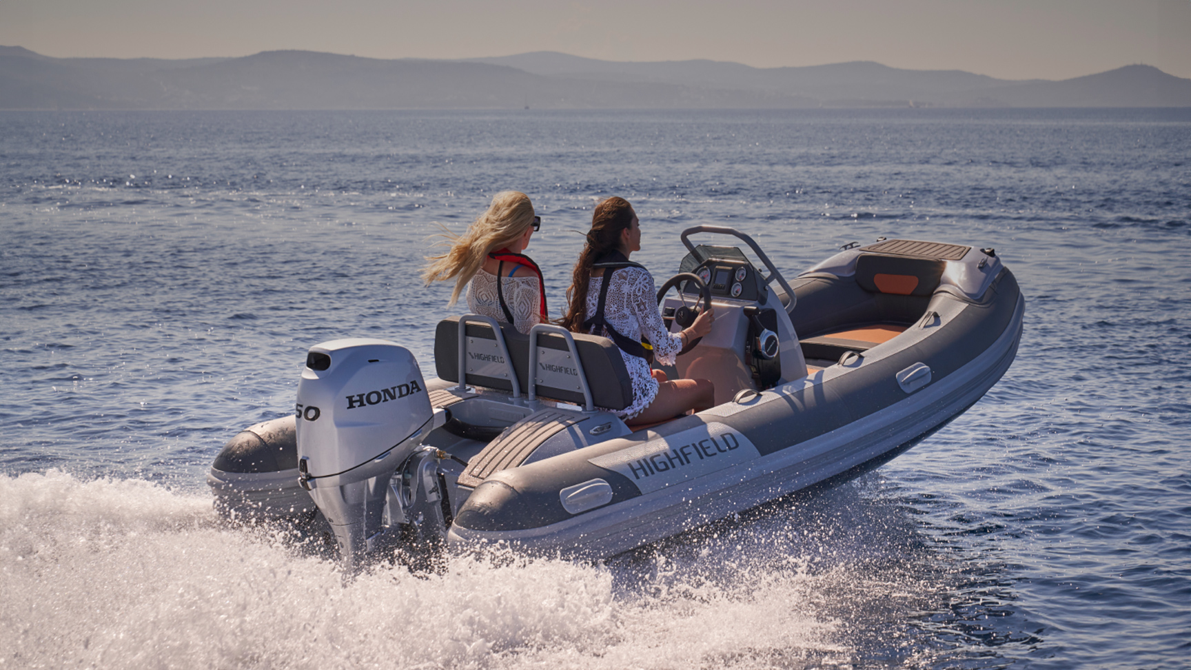 Zwei Models auf einem Highfield-Boot mit Honda BF50-Motor in maritimer Umgebung.