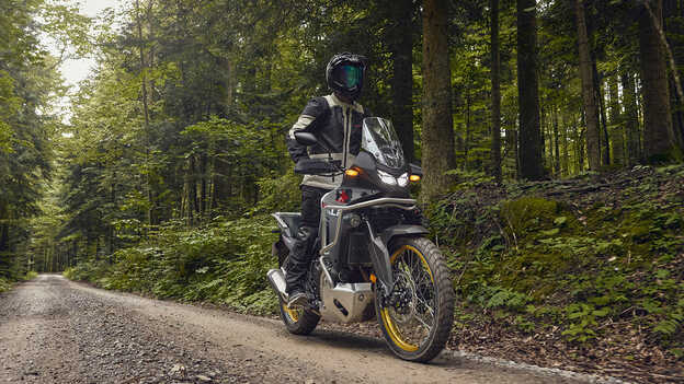 Das Model fährt eine Honda XL750 Transalp in einem Waldgebiet.