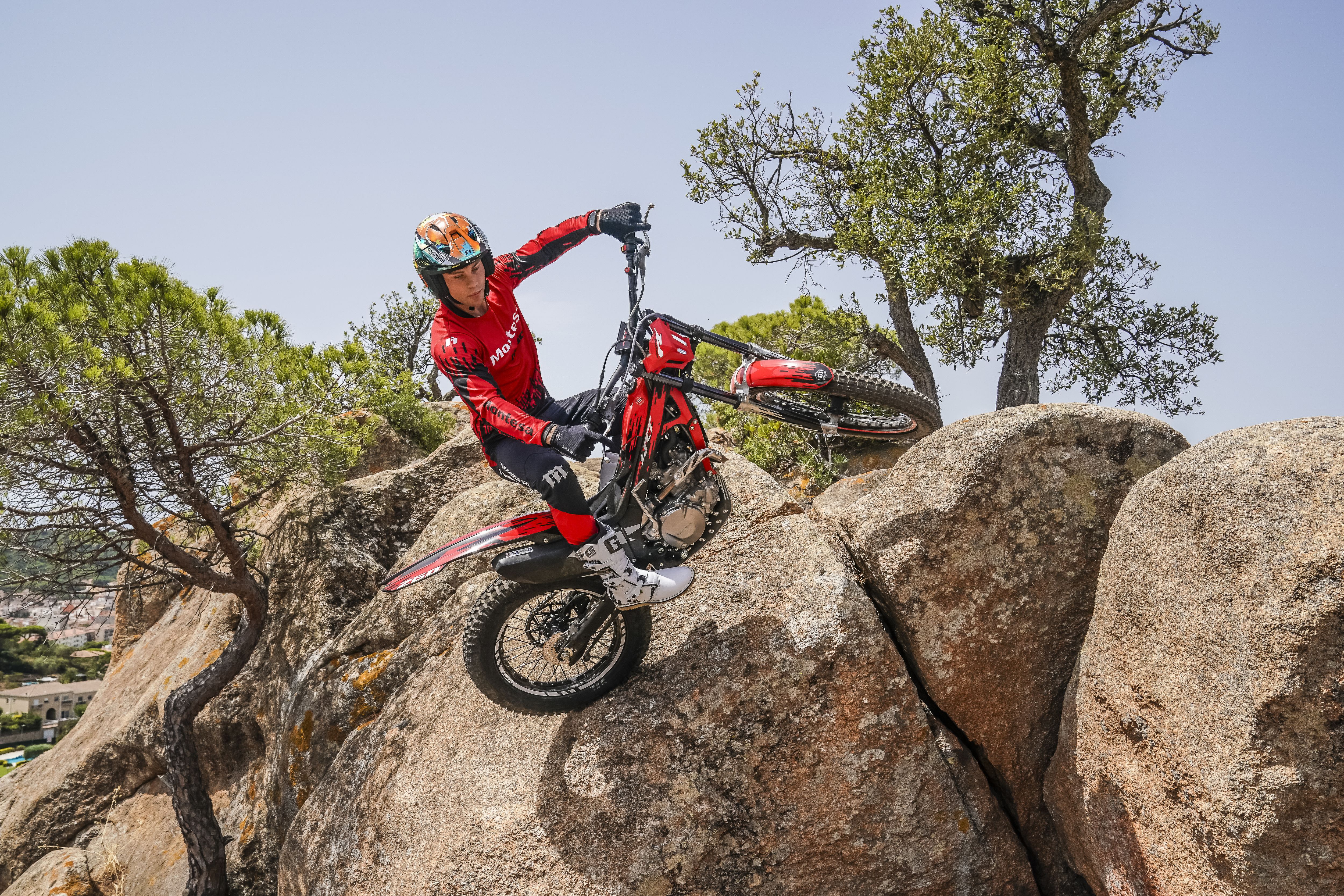 Ein Motorradfahrer, der an einem sonnigen Tag mit einem roten Motorrad der Marke Montesa Cota 4RT 260R über steile Felsbrocken fährt.