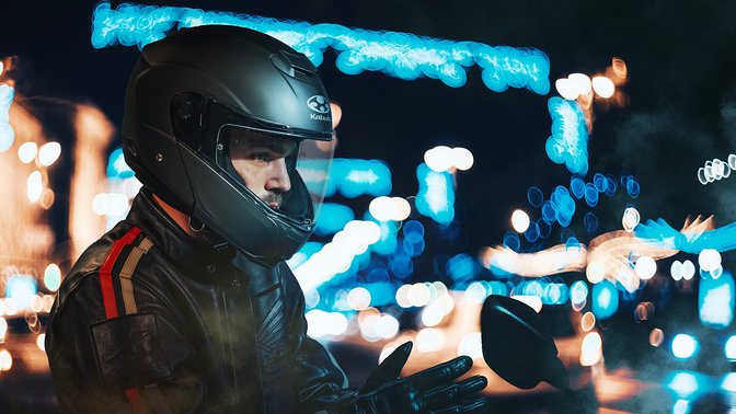 Helm Honda Kabuto, Aeroblade V – Flat Black – aufgesetzt, 3/4-Frontansicht rechts, auf dem Kopf eines Motorradfahrers, in der Stadt bei Nacht