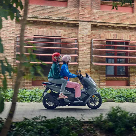 Seitenaufnahme von Models, die den PCX125 in der Stadt fahren.