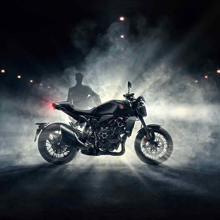 Honda CB1000R Black Edition von rechts, Fahrer steht bei nächtlichem Nebel hinter dem schwarzen Fahrzeug