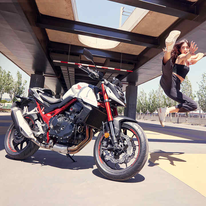 Tänzerin, die neben einer Honda CB750 Hornet in die Luft springt.