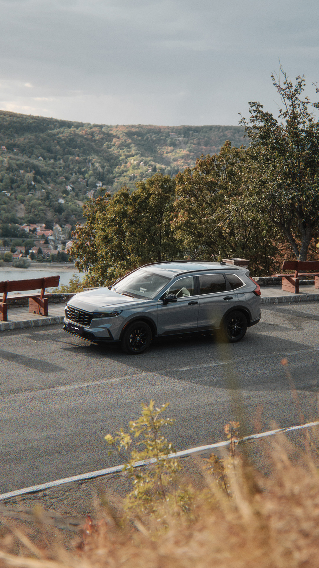 Ein grauer CR-V, der auf einer Strasse am Seeufer entlangfährt, im Hintergrund sind Berge zu sehen