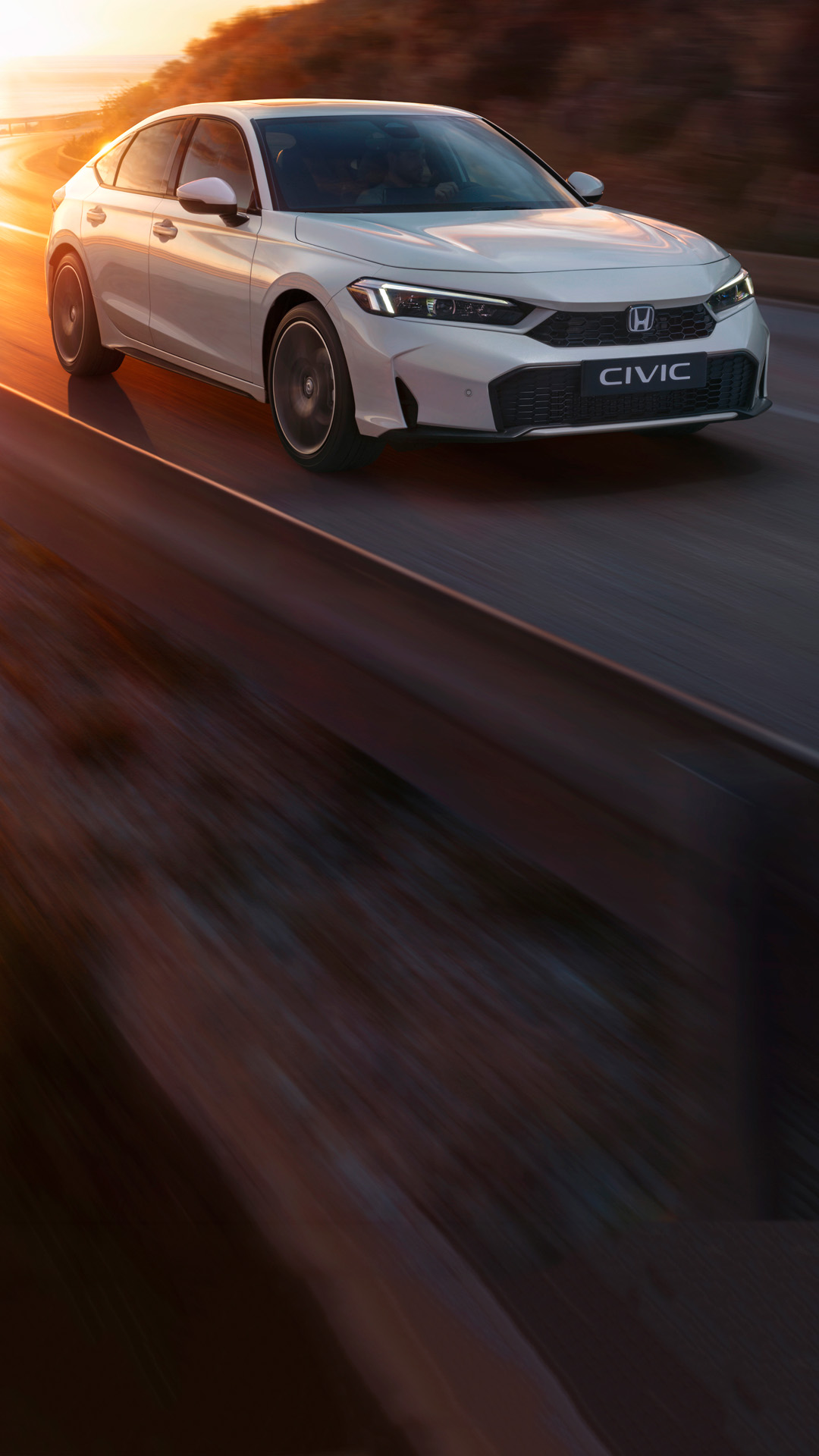 Ein weisser Civic Hybrid fährt auf einer Strasse, im Hintergrund sind der Sonnenuntergang und das Meer zu sehen
